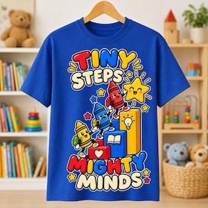May include: A royal blue short-sleeve t-shirt featuring a colorful graphic of three anthropomorphic crayons climbing blocks. The text reads "TINY STEPS" at the top and "MIGHTY MINDS" at the bottom, accompanied by a smiling yellow star icon.