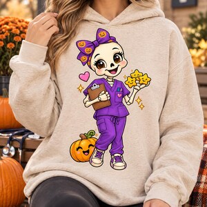 May include: A beige hooded sweatshirt featuring a graphic of a cartoon skeleton dressed in purple medical scrubs, a purple bow with pumpkin patterns, holding a brown clipboard and yellow stars, standing next to a smiling orange pumpkin.