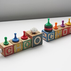 May include: Wooden blocks spelling out the word "CHOO CHOO" with colorful game pieces on top.