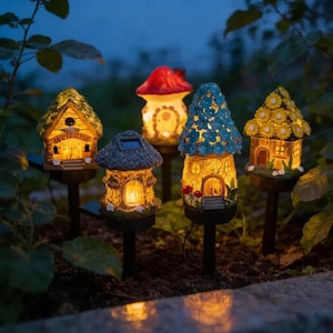 Pode incluir: Cinco luzes solares de jardim em forma de casas em miniatura e um cogumelo. As estruturas apresentam interiores iluminados, com designs que incluem uma casa amarela com uma placa welcome, um cogumelo vermelho e casas com telhados de flores azuis ou amarelas.