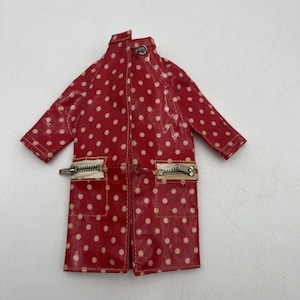 May include: A red raincoat with a white polka dot pattern, featuring long sleeves, a high collar with a single metal snap button closure, and two front pockets with silver-toned metal zippers and white fabric trim along the pocket openings.