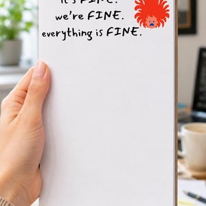 May include: A white rectangular notepad featuring the black printed text it's FINE. we're FINE. everything is FINE. and a small graphic of a cartoon character with wild, spiky red hair and a distressed blue facial expression in the top right corner.