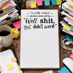 May include: A white rectangular notepad with black text that reads, I'm pretty confident my last words will be Well shit, that didn't work. The notepad features horizontal lines for writing and is positioned vertically on a desk surface.