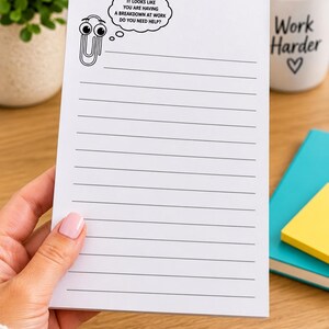 May include: A white rectangular notepad with horizontal black lines. The top left corner features a cartoon paperclip character with a thought bubble containing the text: IT LOOKS LIKE YOU ARE HAVING A BREAKDOWN AT WORK DO YOU NEED HELP?