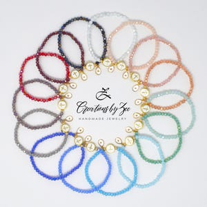 May include: A circular arrangement of twelve beaded bracelets in various colors, including red, blue, green, and white. Each bracelet features a small gold-toned charm with a white cross emblem. The text Creations by Zee Handmade Jewelry is centered.