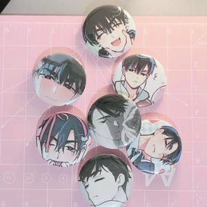 Könnte beinhalten: Sieben runde Ansteckbuttons mit verschiedenen Anime-Illustrationen einer Figur mit dunklem Haar. Jeder Button zeigt einen anderen Gesichtsausdruck, darunter lächelnd, zwinkernd und neutral, dargestellt in einem farbenfrohen, grafischen Stil.