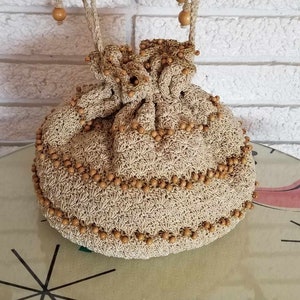 May include: A beige crocheted drawstring bag with brown wooden beads. The bag is hanging from two hooks on a white brick wall.