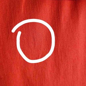 May include: Close-up of a red fabric shirt with a textured weave. The fabric has a subtle sheen and a smooth, even surface.