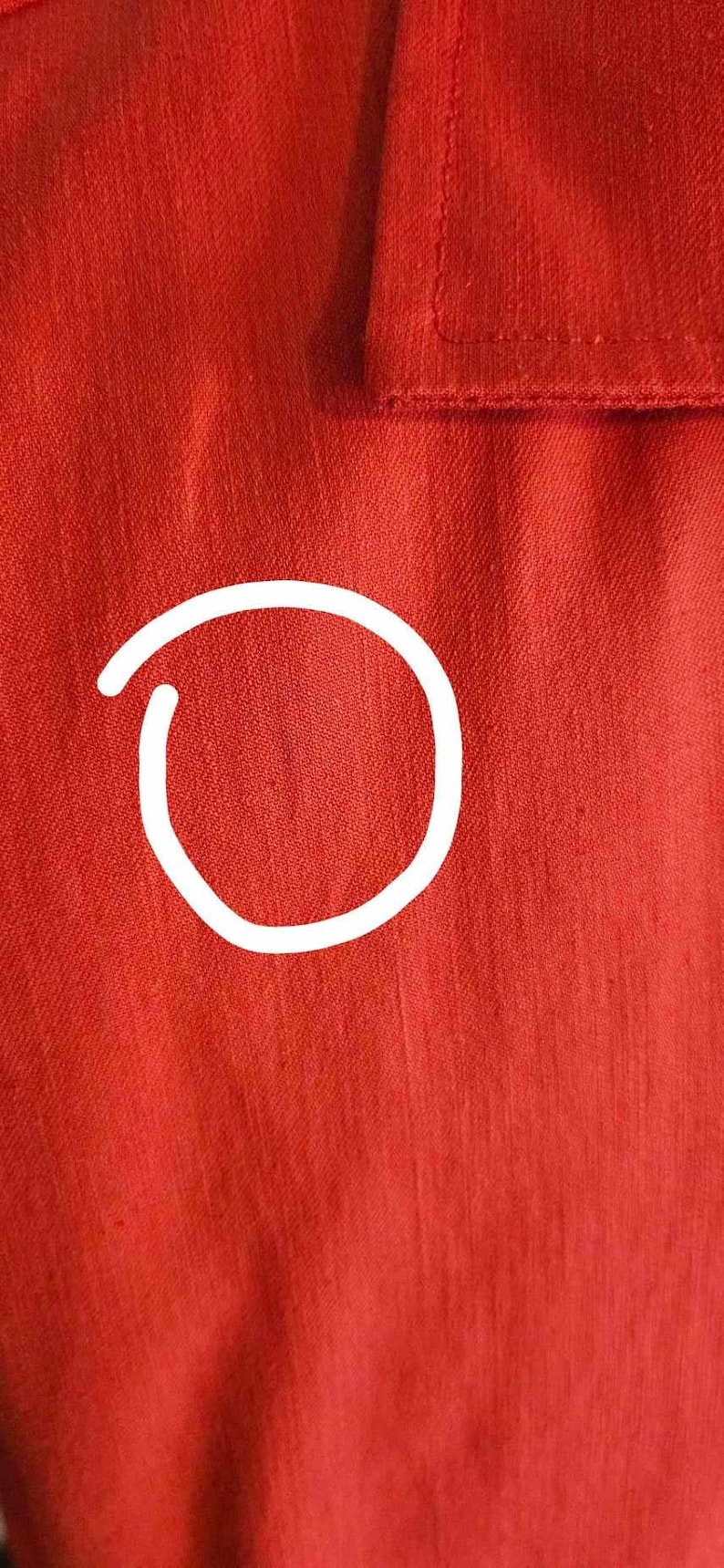 May include: Close-up of a red fabric shirt with a textured weave. The fabric has a subtle sheen and a smooth, even surface.