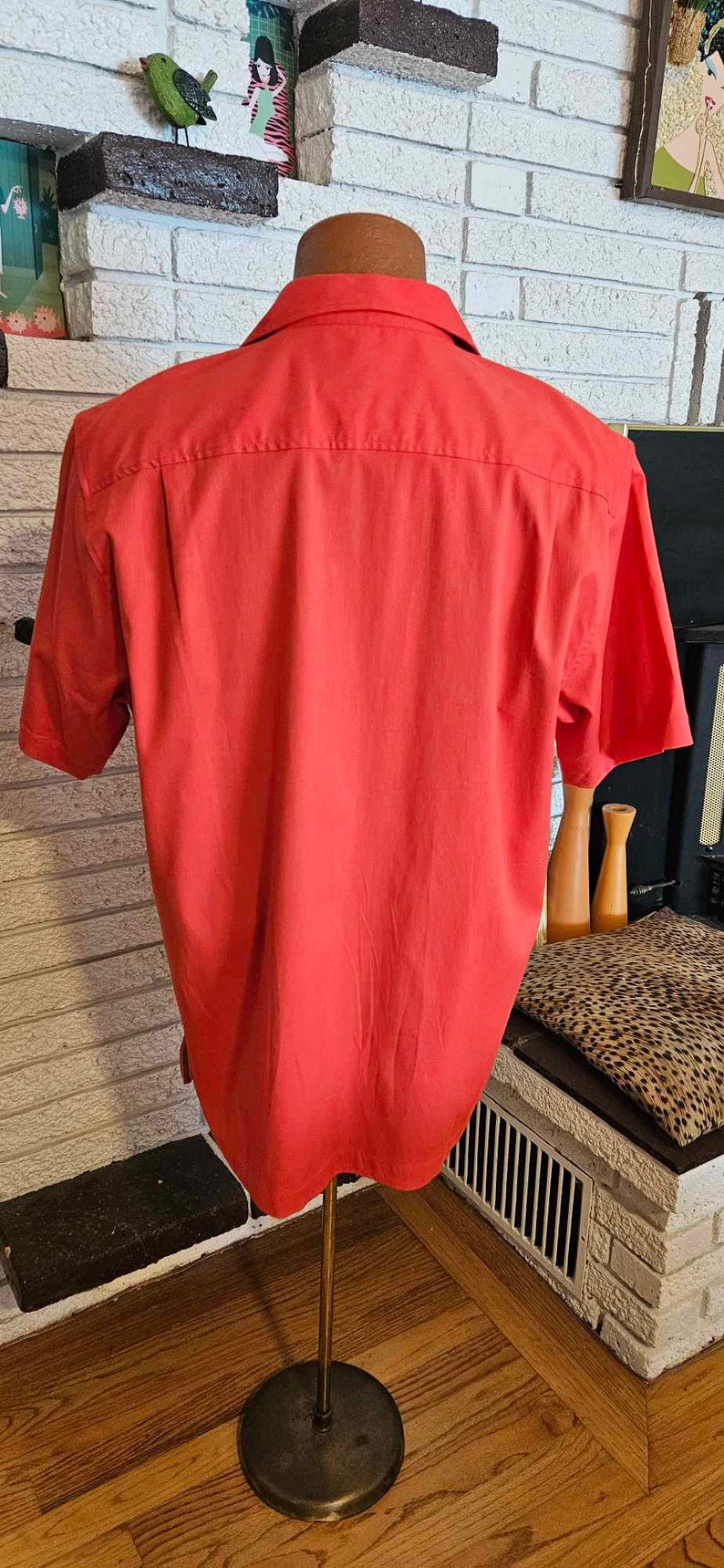 May include: A red short-sleeved button-down shirt on a mannequin. The shirt is made of a smooth, lightweight fabric.