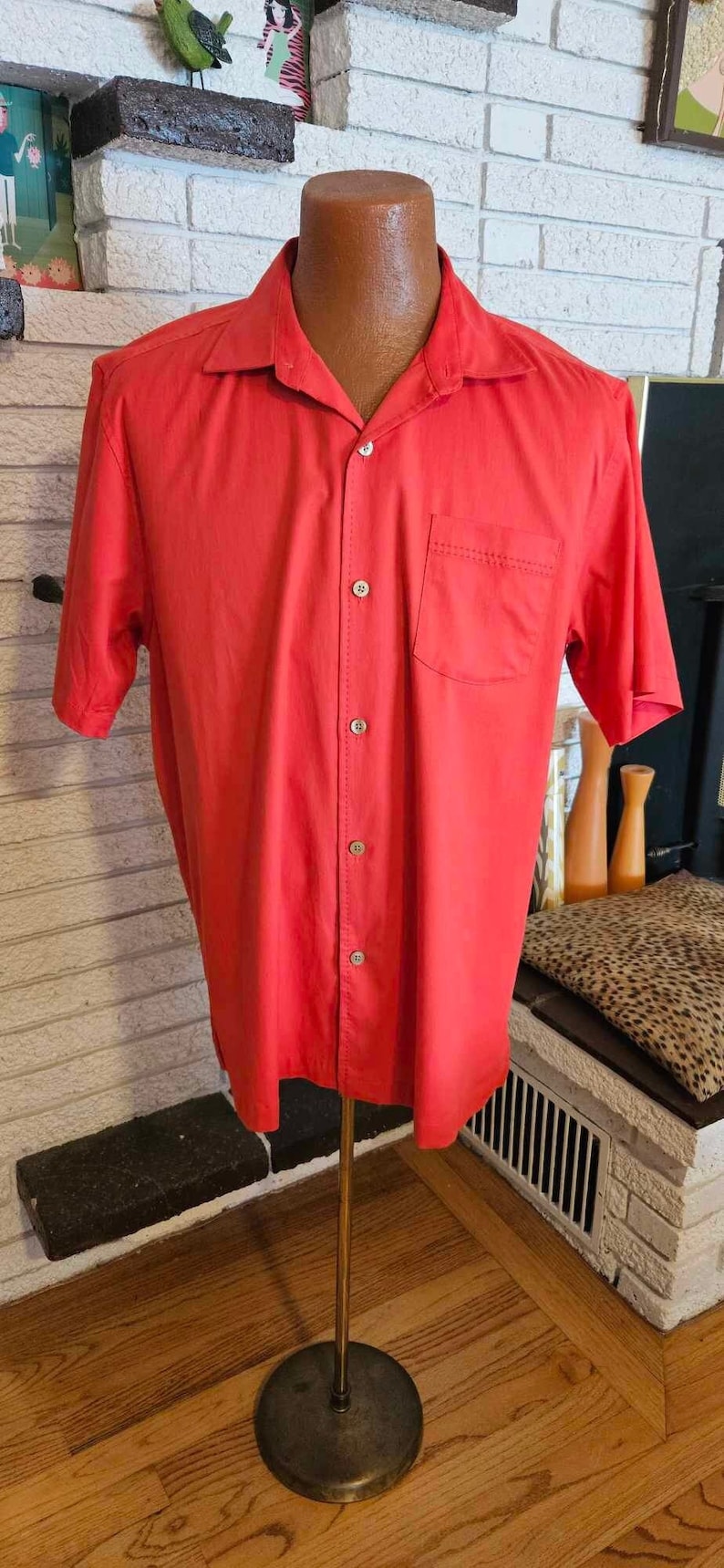 May include: A red short-sleeved button-down shirt with a single chest pocket. The shirt is on a mannequin and has a collar.