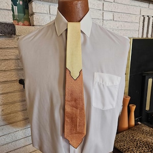 May include: A brown and yellow patterned tie with a black trim. The tie is on a white shirt.