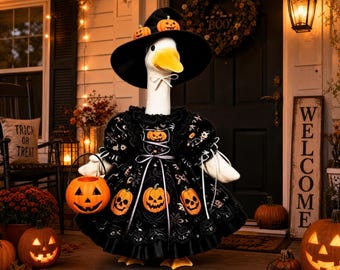 May include: A white goose figurine wearing a black witch hat adorned with small orange pumpkins and a black dress featuring a pumpkin pattern. The goose holds a small orange plastic jack-o'-lantern bucket in its wing, standing on a porch.