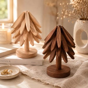 May include: Two decorative tree sculptures crafted from wood, one in a light natural finish and one in a darker brown tone. Each tree features a central cylindrical trunk mounted on a circular base, with multiple layered, petal-shaped wooden slats.