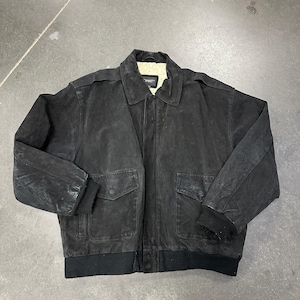 May include: A black suede bomber jacket featuring a fold-down collar, a front zipper closure, two large flap pockets, and black ribbed knit cuffs and hem. The interior is lined with a cream-colored fleece material, and a brand label is visible.