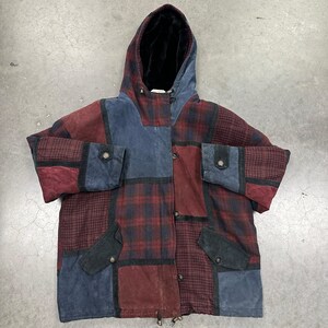 May include: A hooded jacket featuring a patchwork design of blue and burgundy suede panels mixed with dark plaid fabric. The garment includes a black interior lining, long sleeves with buttoned cuffs, two front pockets with flaps, and a front button closure.