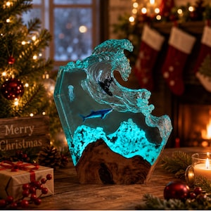May include: A resin sculpture featuring a translucent blue ocean wave crashing over a glowing turquoise base. Inside the clear resin are miniature figures of a shark, a jellyfish, and a surfer on a board, all set within a natural wood frame.