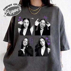 May include: A charcoal gray t-shirt featuring a Comfort Colors Pepper label and a graphic print of four black and white photographs of a person in various poses, accented with purple stars, a crown, sparkles, and heart icons.