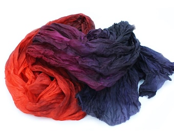 May include: A crumpled fabric scarf in shades of red, purple, and blue. The scarf is made of a soft, flowing material and has a gradient color effect.
