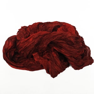 May include: A deep red fabric scarf is crumpled and piled on a white surface.