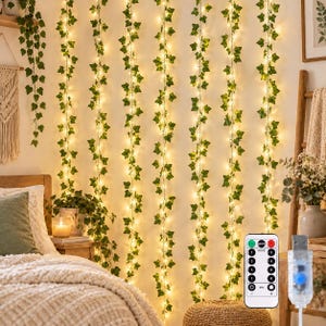 May include: Multiple vertical strands of artificial green ivy vines intertwined with warm white LED fairy lights. The set includes a remote control with various mode and dimming settings, and a USB connector for power, creating a glowing wall display.