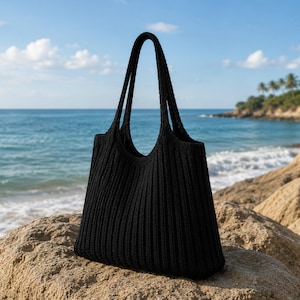 Peut inclure: Un sac fourre-tout noir uni présentant une texture en tricot côtelé vertical. Le sac est doté de deux anses intégrées et d'une ouverture large. La conception est uniforme, mettant en valeur une couleur noire profonde et une forme en tissu souple.