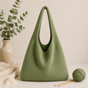 May include: A sage green knitted hobo bag featuring a structured triangular silhouette with a single integrated handle. The bag is crafted from a dense, uniform knit fabric, showcasing a clean, minimalist design with a wide opening at the top.