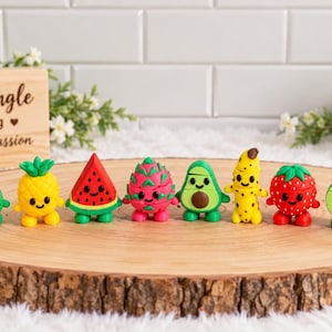 May include: A collection of ten small, colorful fruit-shaped figurines with smiling faces and small feet, arranged in a row. The fruits include an apple, papaya, pineapple, watermelon, dragon fruit, avocado, banana, strawberry, lime, and lemon.