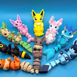 May include: A collection of ten articulated, multi-colored plastic figures resembling fictional creatures. Each figure features a distinct color scheme, including yellow, pink, blue, brown, orange, and black, with segmented tails and small paws.