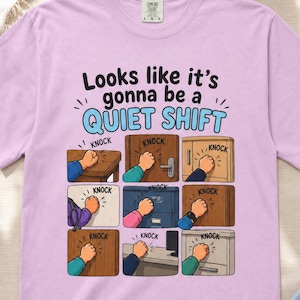 以下が含まれることがあります： ライトパープルのTシャツ。中央には「Looks like it's gonna be a QUIET SHIFT」という文字と、テーブル、ドア、キャビネット、引き出しなど、様々な場所を拳でノックしている様子を描いた9つのイラストがグリッド状に配置されています。