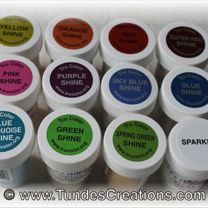May include: Twelve small jars of paint with Tru Color labels. The jars are arranged in three rows of four. The labels are white with black text and show different colors of paint, including yellow, orange, red, super red, pink, purple, sky blue, blue, blue turquoise, green, spring green, and sparkle.