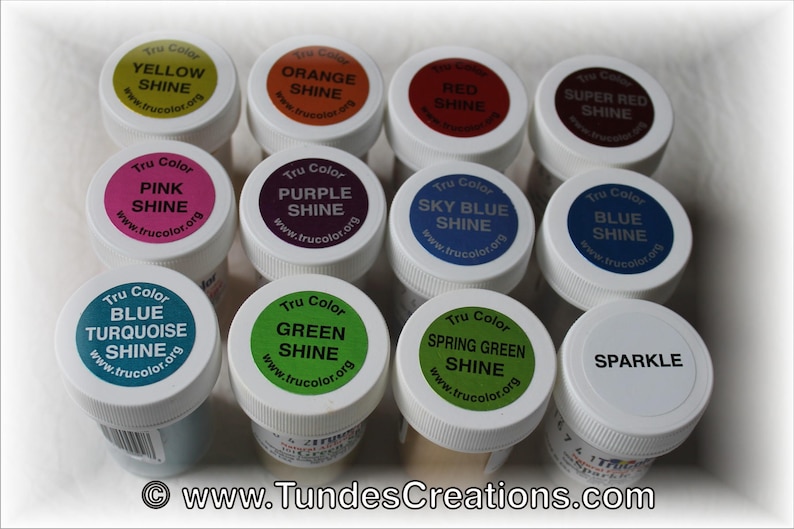 May include: Twelve small jars of paint with Tru Color labels. The jars are arranged in three rows of four. The labels are white with black text and show different colors of paint, including yellow, orange, red, super red, pink, purple, sky blue, blue, blue turquoise, green, spring green, and sparkle.