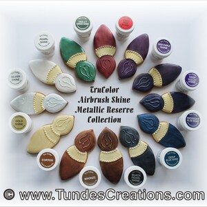May include: A collection of 12 TruColor Airbrush Shine Metallic Reserve colors in small jars. The jars are arranged in a circle around a set of 12 painted gingerbread cookies shaped like paintbrushes. The colors include: Holly Green Shine, Deep Red Shine, Pearl Shine, Deep Purple Shine, Deep Violet Shine, Silver Shine, Gold Shine, Midnight Blue Shine, Copper Shine, Bronze Shine, Black Pearl Shine, and Deep Blue Shine.