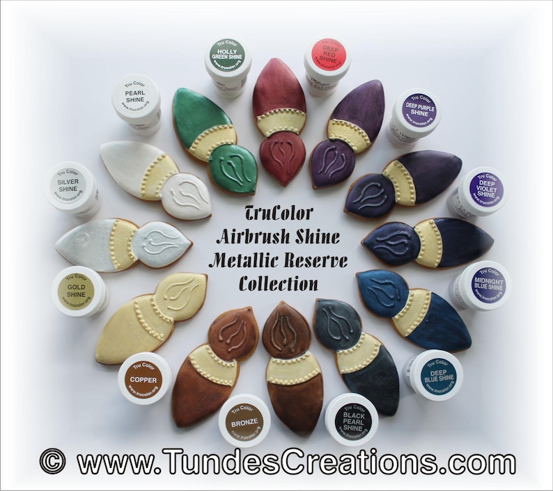 May include: A collection of 12 TruColor Airbrush Shine Metallic Reserve colors in small jars. The jars are arranged in a circle around a set of 12 painted gingerbread cookies shaped like paintbrushes. The colors include: Holly Green Shine, Deep Red Shine, Pearl Shine, Deep Purple Shine, Deep Violet Shine, Silver Shine, Gold Shine, Midnight Blue Shine, Copper Shine, Bronze Shine, Black Pearl Shine, and Deep Blue Shine.