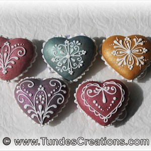 May include: Five heart-shaped cookies decorated with white icing and intricate designs. The cookies are in shades of pink, purple, teal, and gold.