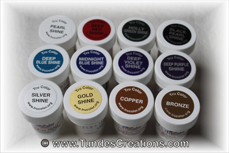 May include: A collection of 10 small, round, white plastic jars with screw-on lids. Each jar contains a different color of paint with a Tru Color label and a website address. The colors include deep blue shine, midnight blue shine, deep violet shine, deep purple shine, silver shine, gold shine, copper, bronze, pearl shine, and deep red shine.