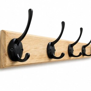 May include: A rectangular light-colored wooden wall rack featuring five matte black metal double hooks. Each hook is secured to the wood base with two visible black screws, providing a dual-prong design for hanging items in a linear arrangement.