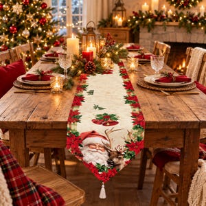 Puede incluir: Un camino de mesa de tela color crema con un diseño estampado de Papá Noel, un reno, flores de pascua rojas y hojas de acebo verdes. El camino tiene un extremo en punta rematado con una borla blanca y un borde decorativo.