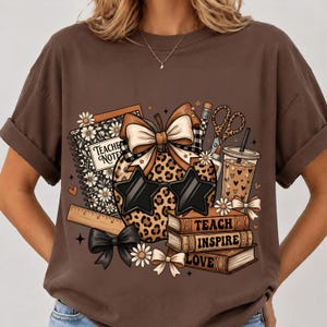 Peut inclure: Un t-shirt marron avec une impression graphique d'une pomme à motif léopard portant des lunettes en forme d'étoile et un nœud. Le motif inclut un carnet marqué Teacher Notes, une règle, des ciseaux, une boisson et des livres marqués Teach, Inspire, Love.
