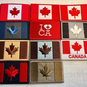 May include: A collection of eleven rectangular embroidered patches featuring various Canadian flag designs, including red and white, blue, brown, and olive color schemes, with some displaying the text I heart CA or CANADA.