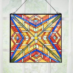 May include: A square stained glass panel featuring a geometric pattern of intersecting lines and triangles in shades of yellow, orange, red, blue, and green. The panel is framed in black metal and suspended by a thin metal chain for hanging display.
