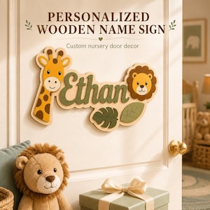 Pode incluir: Uma placa de madeira com o nome Ethan em letra cursiva verde-escura, ladeada por uma girafa amarela e um leão castanho. A placa inclui dois recortes de folhas verdes e o texto PERSONALIZED WOODEN NAME SIGN Custom nursery door decor.
