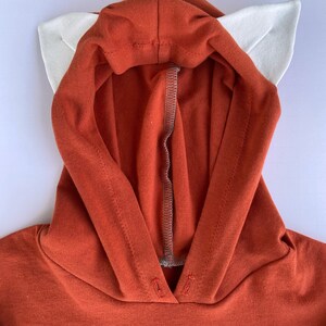May include: A red hooded sweatshirt with white ears attached to the hood. The sweatshirt is made of a soft, comfortable fabric.