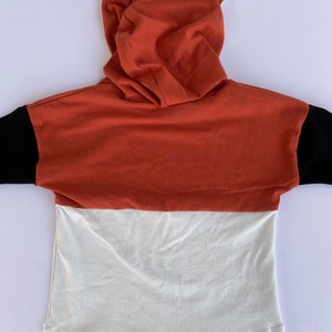 May include: A red, white and black hooded sweatshirt with fox ears. The sweatshirt has a long sleeve and a relaxed fit.