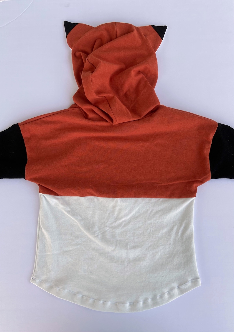 May include: A red, white and black hooded sweatshirt with fox ears. The sweatshirt has a long sleeve and a relaxed fit.