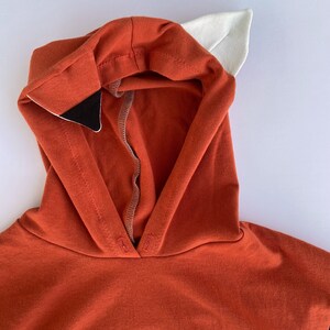 May include: A red hooded sweatshirt with white and black fox ears attached to the hood.
