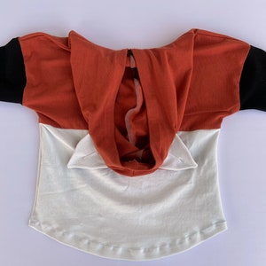 May include: A red and white hooded top with black sleeves. The hood has two small ears on the top.