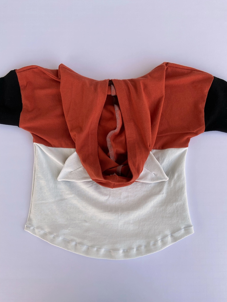 May include: A red and white hooded top with black sleeves. The hood has two small ears on the top.