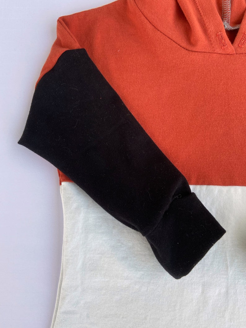 May include: A hooded sweatshirt with a colour block design. The sleeves are black, the top is orange, and the bottom is white.