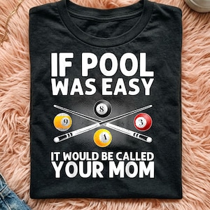 May include: A black t-shirt featuring white text that reads IF POOL WAS EASY IT WOULD BE CALLED YOUR MOM. The graphic includes two crossed pool cues and four billiard balls numbered 8, 9, 3, and 1 arranged in a central cluster design.